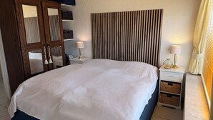 Ein Schlafzimmer mit einem großen Bett, zwei Nachttischen mit Lampen, einem hölzernen Kopfteil und einem Schrank mit Spiegel.