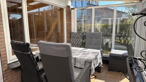 Eine überdachte Terrasse mit Korbmöbeln, einem Tisch mit gemustertem Tischläufer und Blick ins Freie.