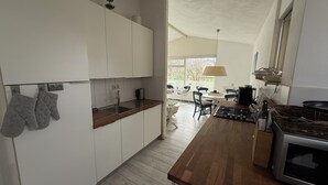 A modern kitchen with white cabinets, a wooden countertop, and a gas stove. There is a dining area with a table and chairs visible through a doorway.