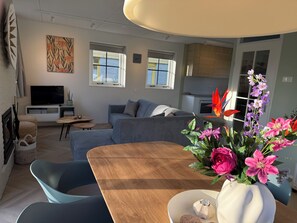 Uma sala de estar moderna com um sofá, uma televisão, uma mesa de jantar com cadeiras e um vaso de flores.