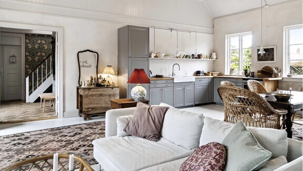 A spacious living area with a sofa, a dining table, a kitchen with grey cabinets, and a staircase leading to another room. - Unique holiday home with history in Bornholm (Svaneke)