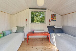 A room with two beds, a table, a window, and a colorful artwork on the wall. - Holiday home with peace, nature and great moments (Jægerspris)
