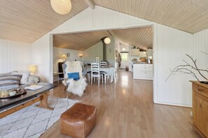A spacious living area with a high ceiling, wooden flooring, a dining table with chairs, a sofa, and a kitchen in the background. - Holiday home with peace, nature and great moments (Jægerspris)