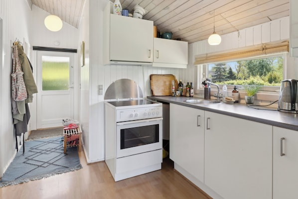 A kitchen with white cabinets, a stove, and a window with a view of greenery. - Holiday home with peace, nature and great moments (Jægerspris)