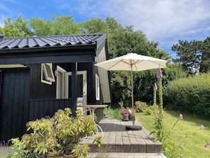 A wooden cabin with a tiled roof, a patio with a table and chairs, and a white umbrella.