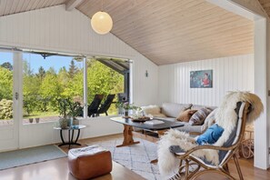 Ein geräumiger Raum mit großem Fenster, Holzbalkendecke, Korbstuhl, Sofa und Tisch mit einer Vase.