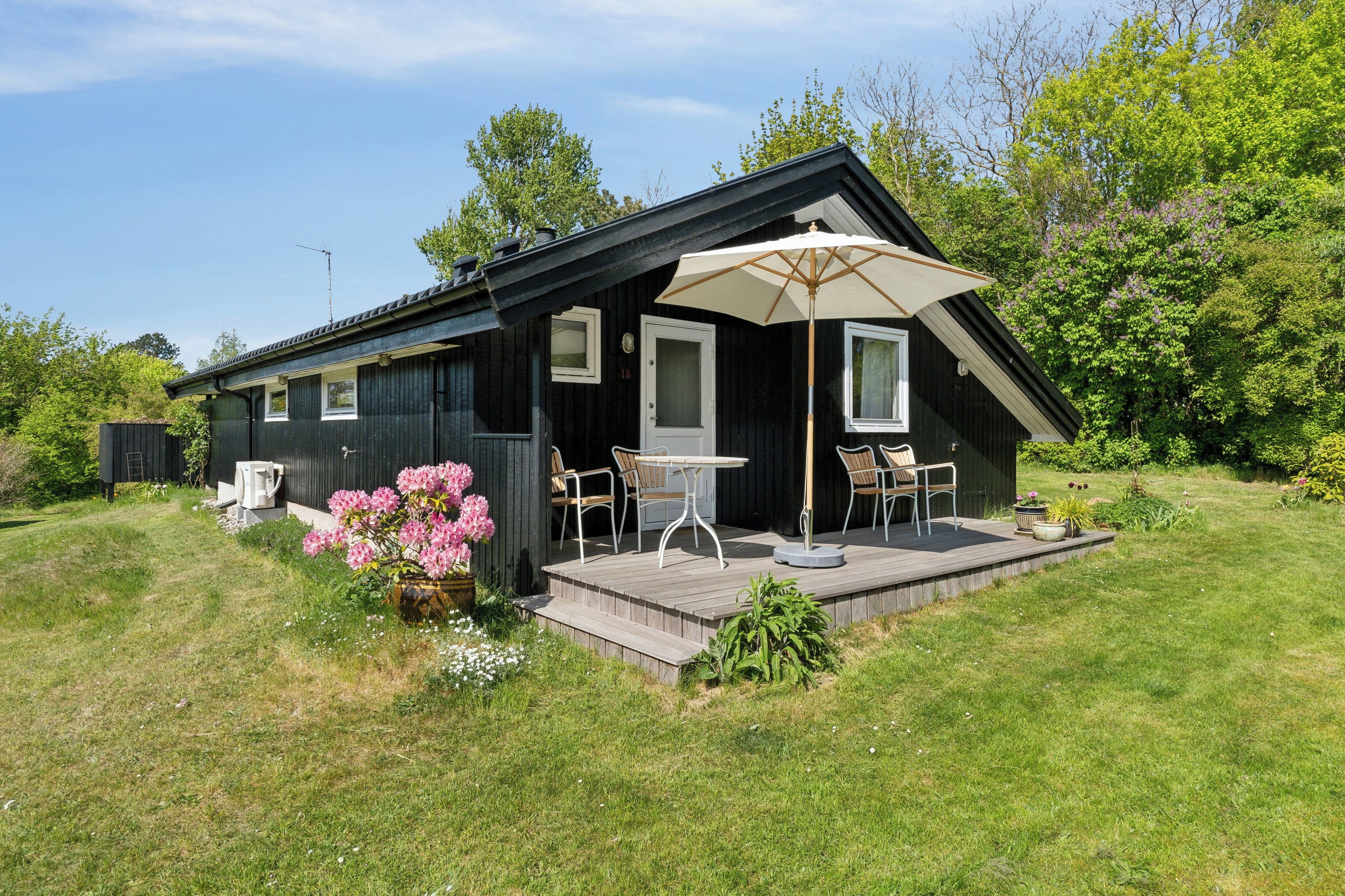 A black wooden house with a patio, two chairs, a table, and an umbrella.