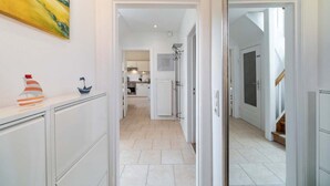 Un pasillo que da a una cocina y comedor con armarios blancos y piso de baldosas.