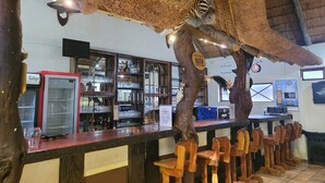 Zona de bar con diseño rústico, que incluye techo de paja, sillas de madera y estanterías con copas y botellas.