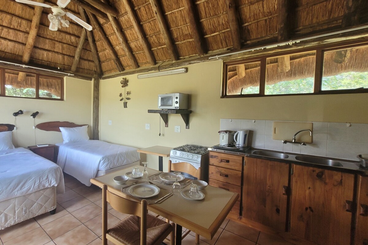 A room with two beds, a table set for dining, a kitchenette, and a ceiling fan.