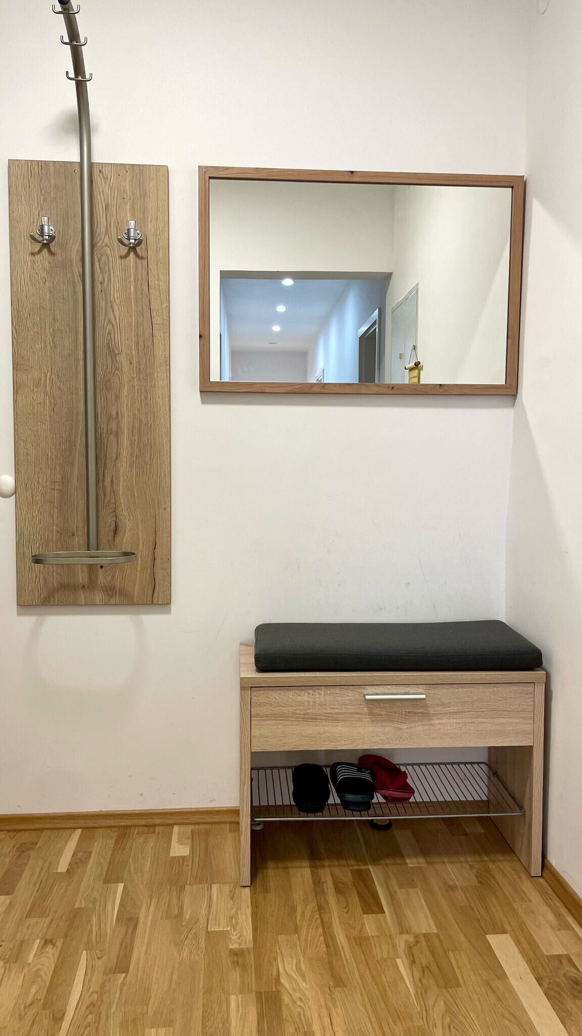 A room with a wooden cabinet, a bench with a storage drawer, and a mirror on the wall.