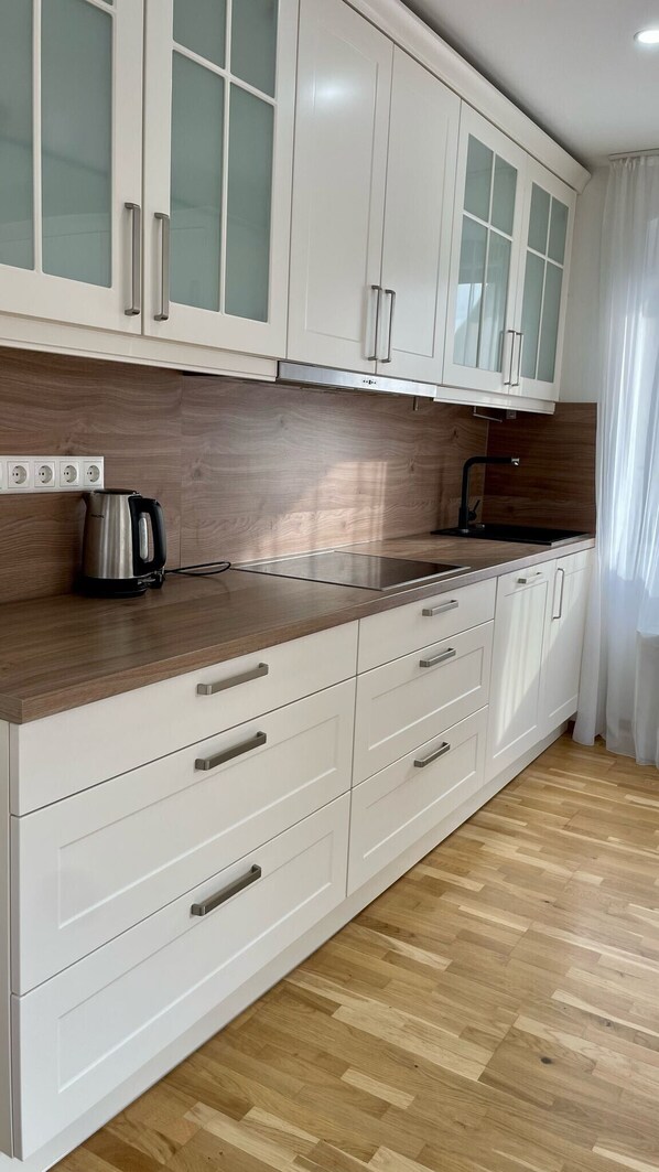 Une cuisine avec des meubles blancs, un plan de travail en bois, une bouilloire et un évier.