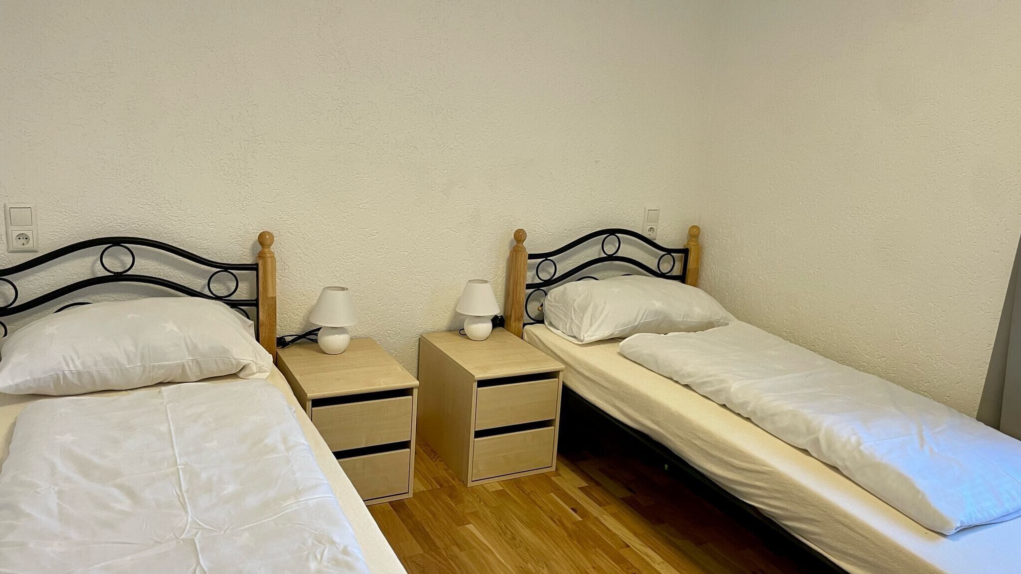Une chambre avec deux lits simples, chacun doté d’une tête de lit en bois et d’une table de chevet avec une lampe.
