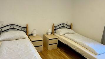 Une chambre avec deux lits simples, chacun doté d’une tête de lit en bois et d’une table de chevet avec une lampe.