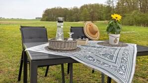 A table set outdoors with a tablecloth, chairs, a basket, a hat, a flower, and a thermos. - Holiday & Worker Apartment Kaiser with Private Terrace and Wi-Fi (Uelzen)