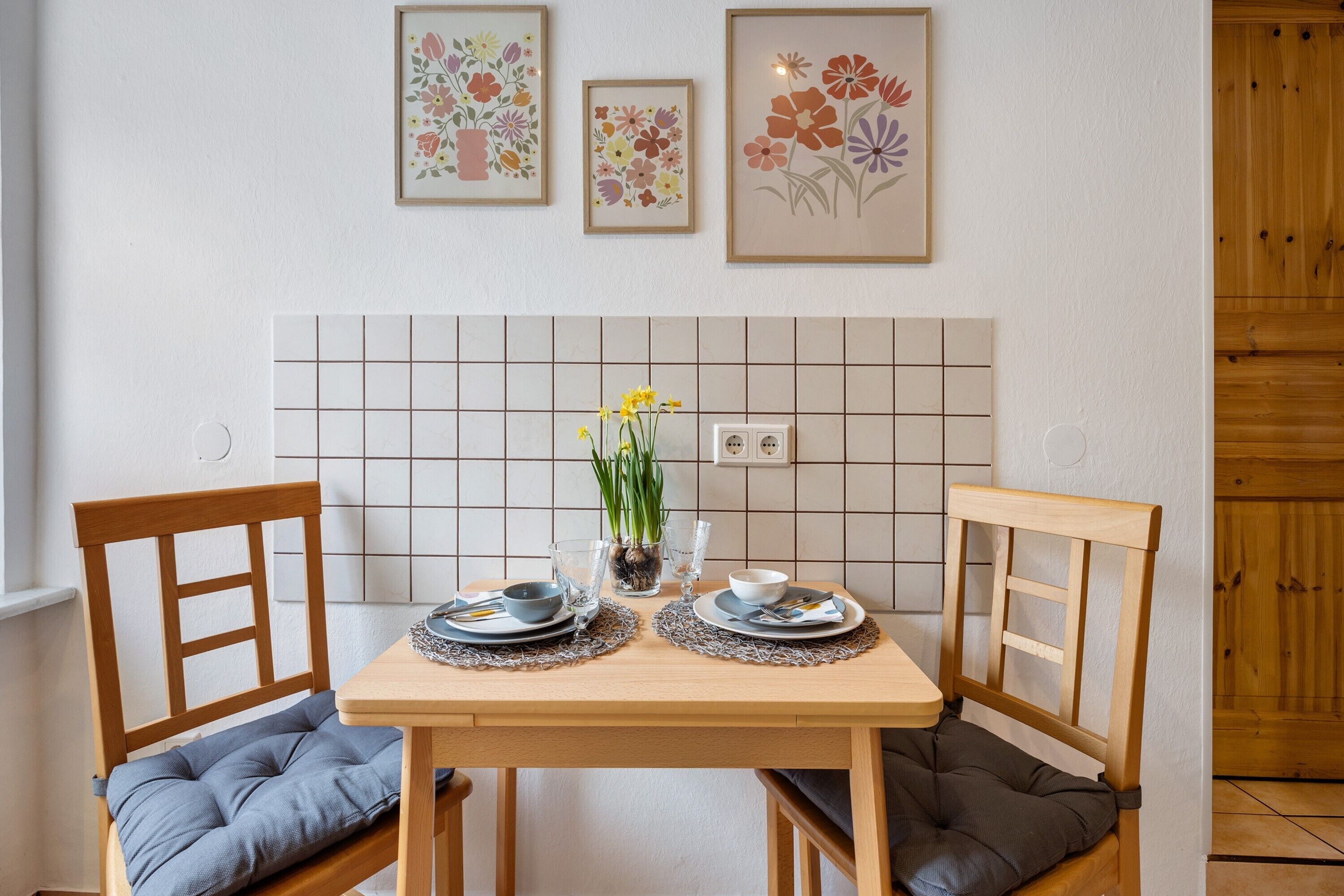 Ein Esstisch mit Stühlen, eine geflieste Spritzschutzwand und gerahmte Blumenbilder an der Wand.