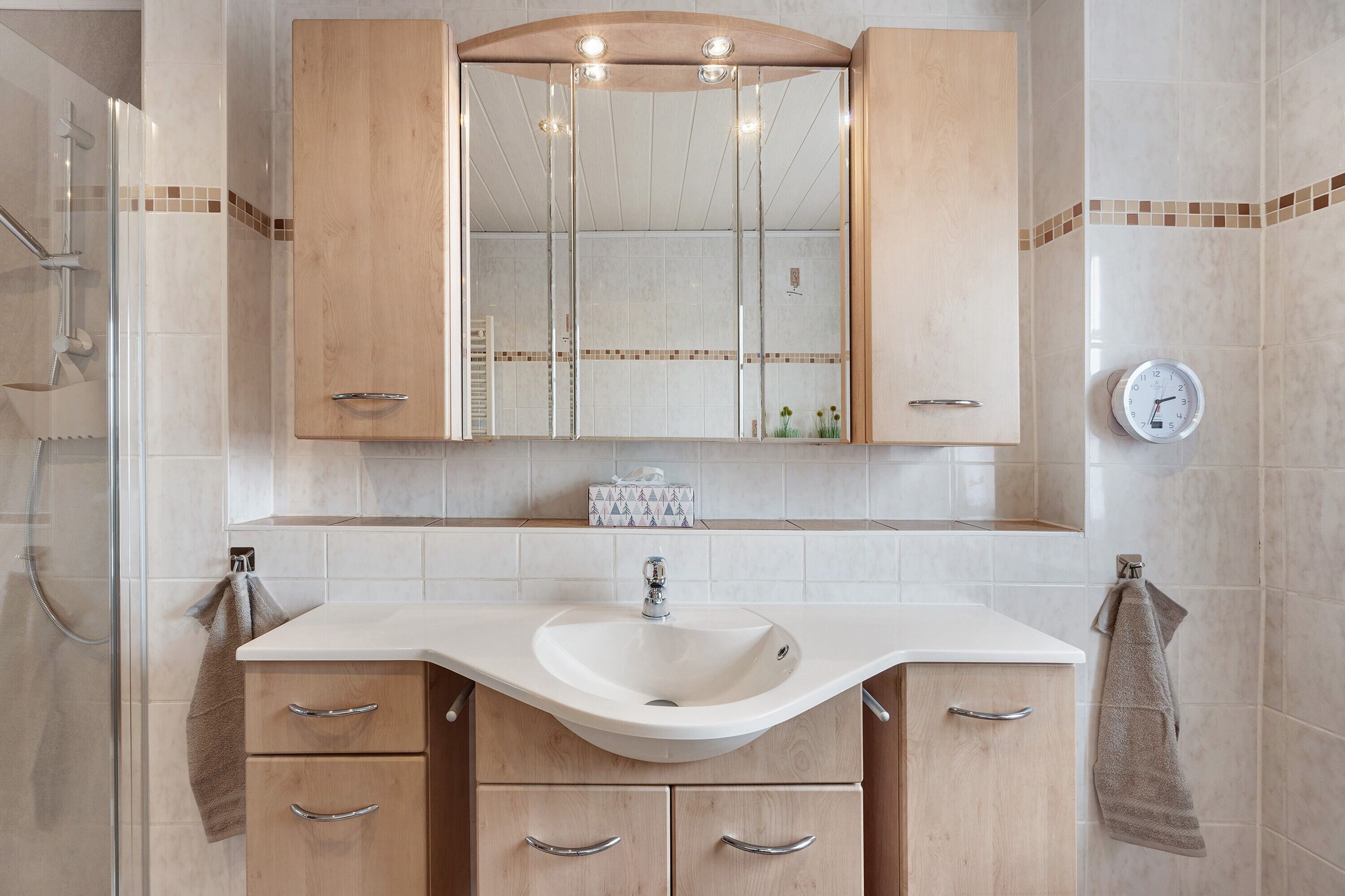 Un baño con lavamanos, espejo y armarios de madera.