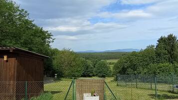 A rural landscape with a wooden shed, a fenced area with a planter box, and a view of distant hills.