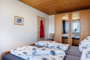 Una stanza con due letti, soffitto in legno, una porta con un cappotto rosso appeso e un quadro appeso al muro.