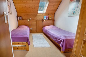 Pieni huone, jossa on kaksi sänkyä, kattovalokuvio, puuseinät, ovi ja hylly kirjoja varten.