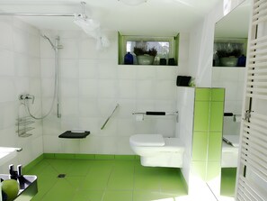 Een badkamer met douche, toilet en wastafel, groene tegels en een raam met planten.
