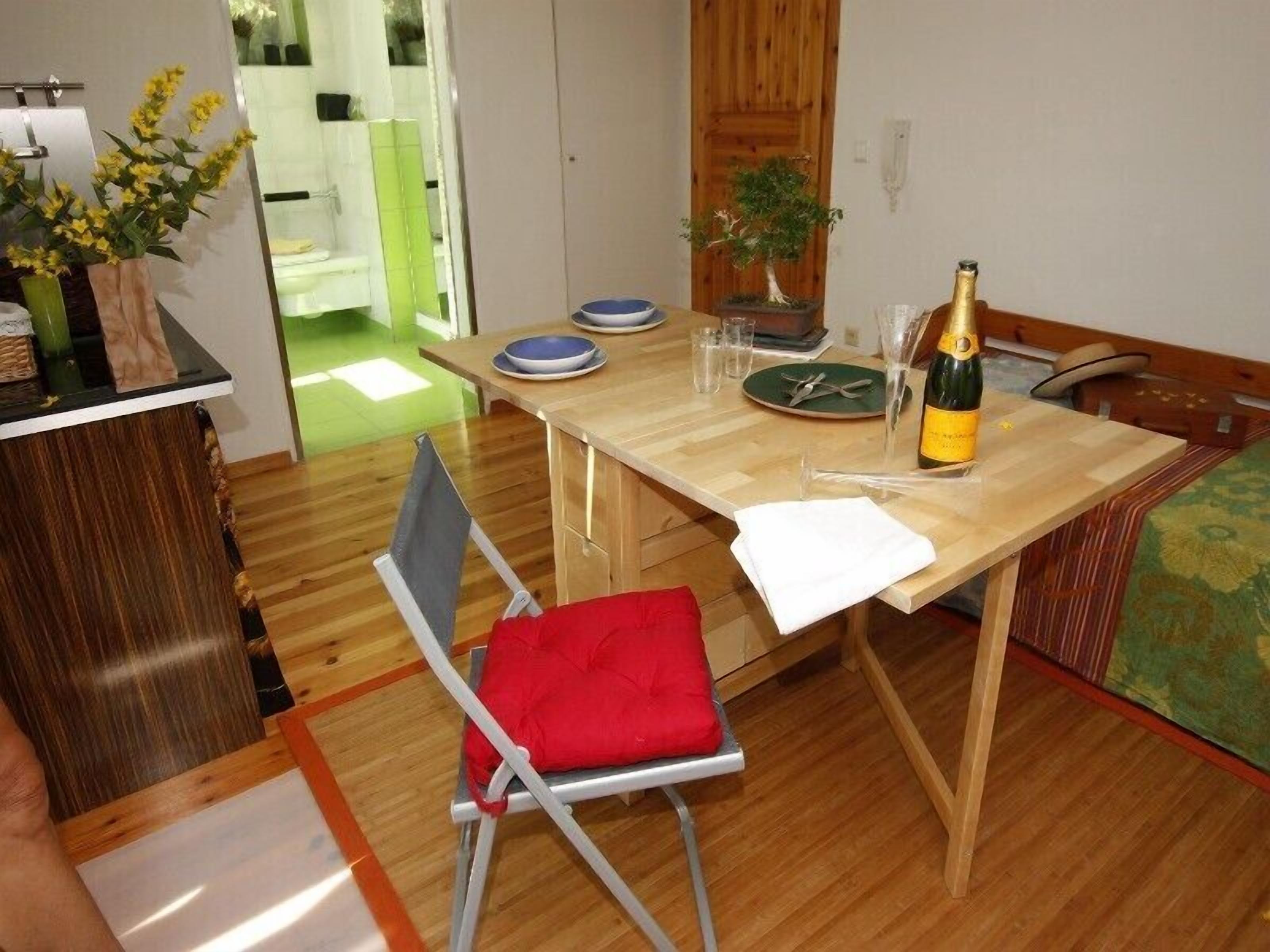 A dining area with a wooden table, chairs, a bottle of champagne, and a small potted plant.