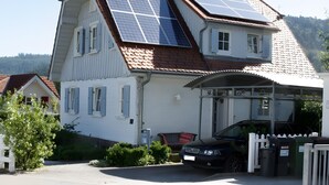 Una casa de dos pisos con paneles solares en el techo, un garaje y una valla de piquete blanca.
