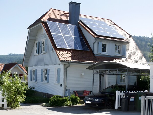 Een woonhuis met twee verdiepingen, zonnepanelen op het dak, een garage en een witte picket fence.