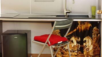A compact kitchen with a sink, a small refrigerator, and a chair with a red cushion.