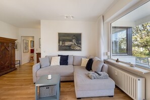 A modern living room with a sectional sofa, a small table, and a large window with a view. - Apartment 'Fallreep' with Private Terrace, Private Garden and Wi-Fi (Lübeck Travemünde)