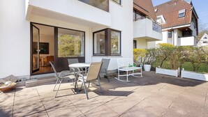 Una casa moderna a due piani con patio, mobili da esterno e un'ampia finestra.