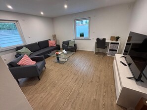 A modern living room with a glass coffee table, two sofas, a TV, and a small desk with a chair.