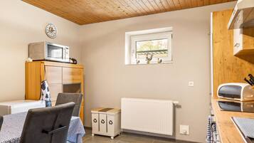 A compact kitchen with a microwave, a small window, a radiator, and a wooden ceiling.