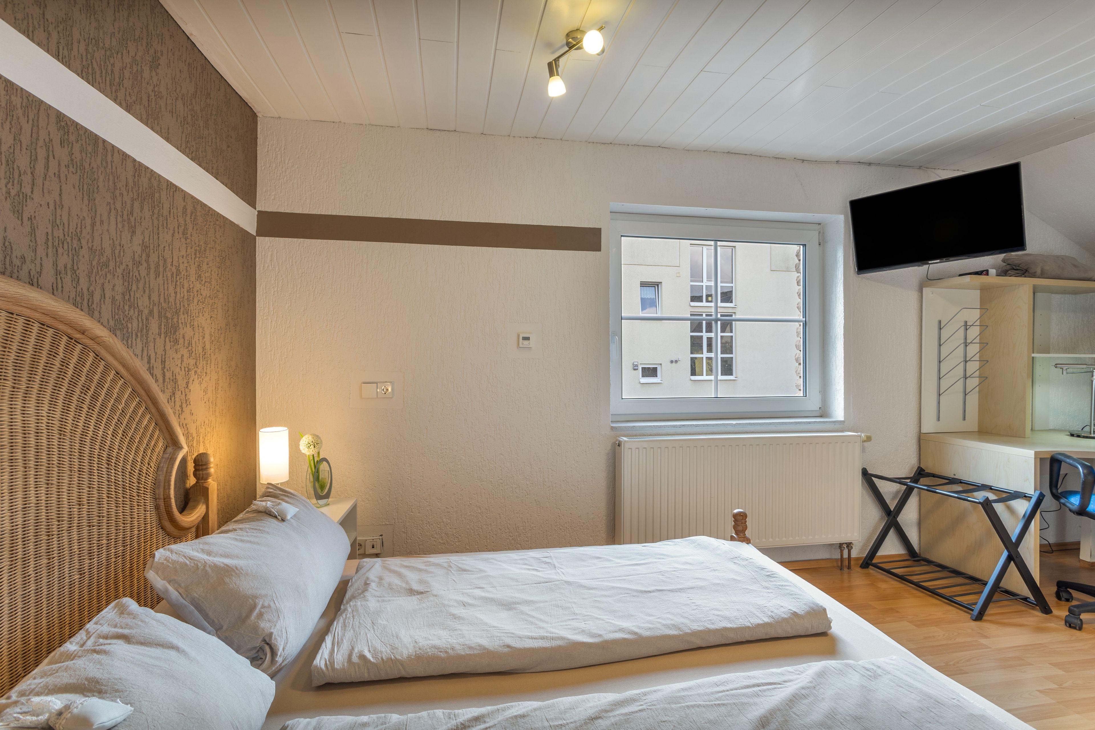 A bedroom with a bed, a window, a television, and a radiator.