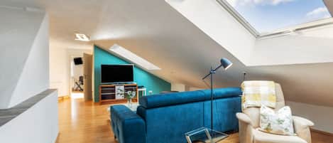 A modern living room with a sloped ceiling, a blue sofa, a small armchair, and a glass table.