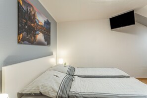 A bedroom with a bed, a painting, a TV, and a nightstand with a lamp. - Vogler Holiday Apartment (Herscheid)