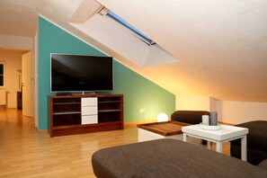 A modern living room with a flat-screen TV on a wooden stand, a small white table with a candle, and a dark-colored sofa.