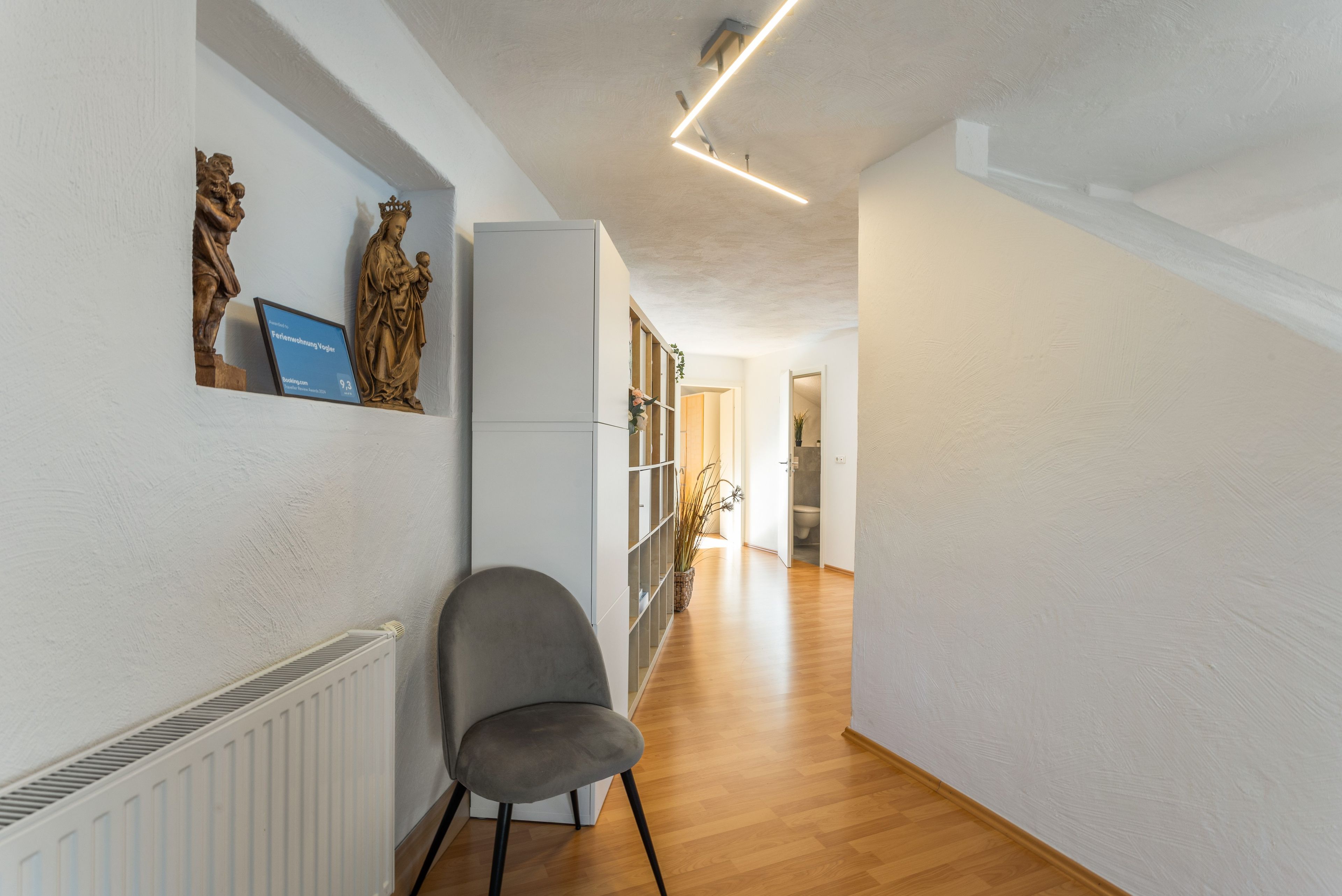 A hallway with a radiator, a grey chair, and a statue on the wall.