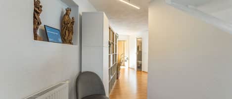 A hallway with a radiator, a grey chair, and a statue on the wall.