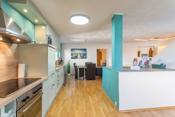 A modern kitchen with a central island, a dining area with a table and chairs, and a view of the living area. - Vogler Holiday Apartment (Herscheid)