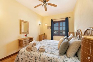 Un dormitorio con cama, ventilador de techo, cómoda, espejo y ventana con cortinas.