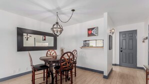 A dining area with a round table and four chairs, a chandelier, a wall-mounted mirror, and a door with a coat rack. - Fashion Square Townhouse | 4 Heated Pools (Scottsdale)