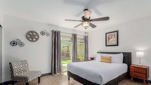 A bedroom with a bed, a chair, a nightstand, a lamp, a ceiling fan, and a window with curtains. - Fashion Square Townhouse | 4 Heated Pools (Scottsdale)