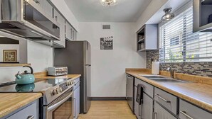 A modern kitchen with grey cabinets, a stainless steel refrigerator, a built-in oven, a wooden countertop, and a window with blinds. - Fashion Square Townhouse | 4 Heated Pools (Scottsdale)