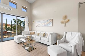 A spacious living room with a white sofa, a glass coffee table, and a view of the outdoors.
