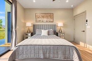 A bedroom with a large bed, two bedside tables, a ceiling light, a door, and a window with curtains.