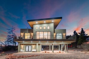 A modern two-story house with a flat roof, large windows, and a balcony.