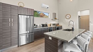 Una cocina moderna con refrigerador de acero inoxidable, horno empotrado y una isla grande con taburetes de bar.