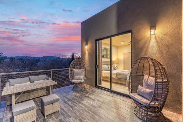 A balcony with wicker furniture, a bed with a sliding door, and a view of the landscape.