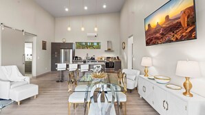 Amplia sala de estar con mesa de comedor, sofás blancos y una cocina al fondo.